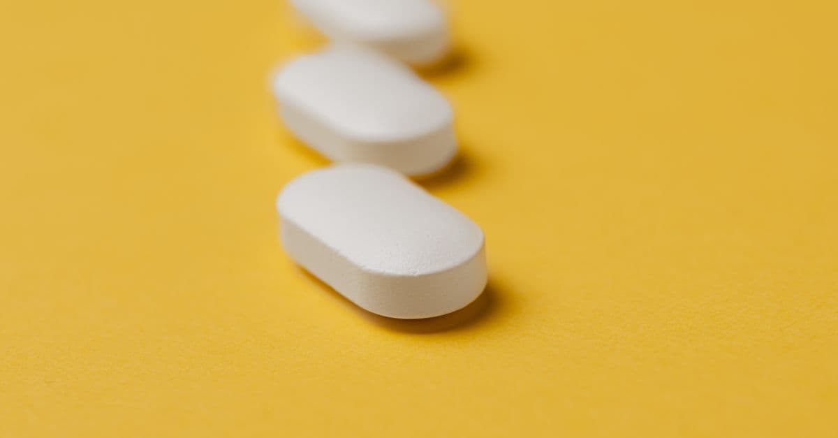 Closeup set of white elliptical medical pills arranged in row on bright yellow plain background