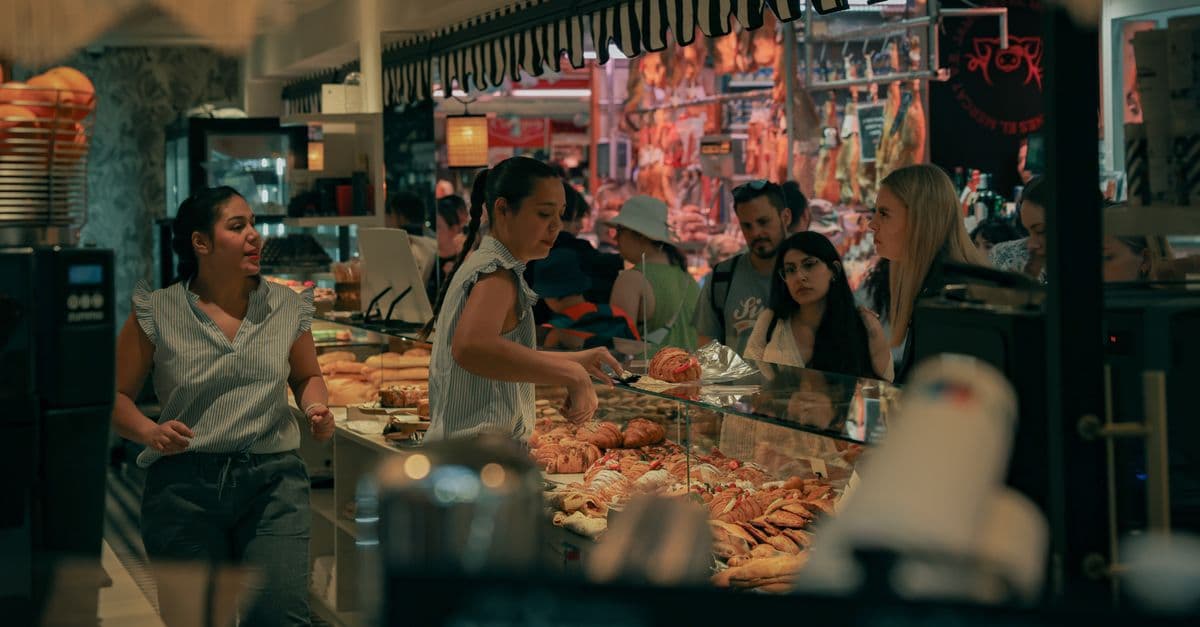 Lively indoor bakery scene in Valencia's bustling market with diverse customers and baked goods.