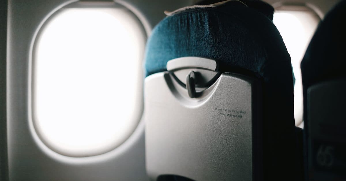 View of an airplane seat with window revealing a bright sky outside.