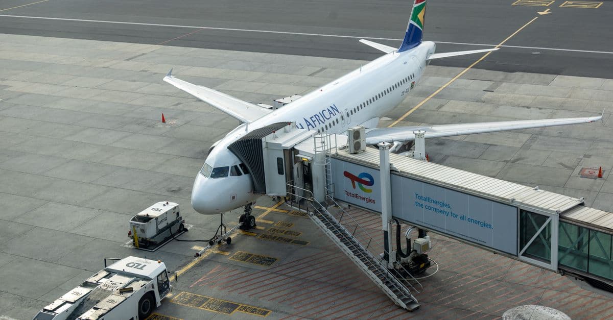 South African Airways aircraft docked at airport gate with passenger bridge connected.