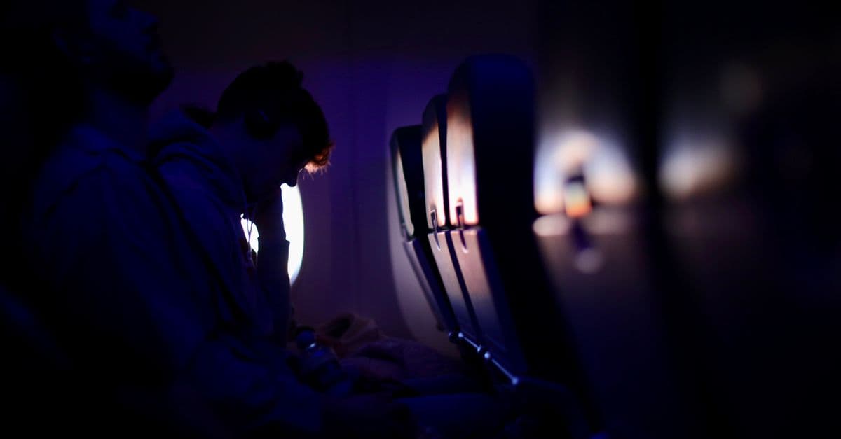 Passengers resting in a dimly lit airplane with purple ambient lighting, showcasing a peaceful travel experience.