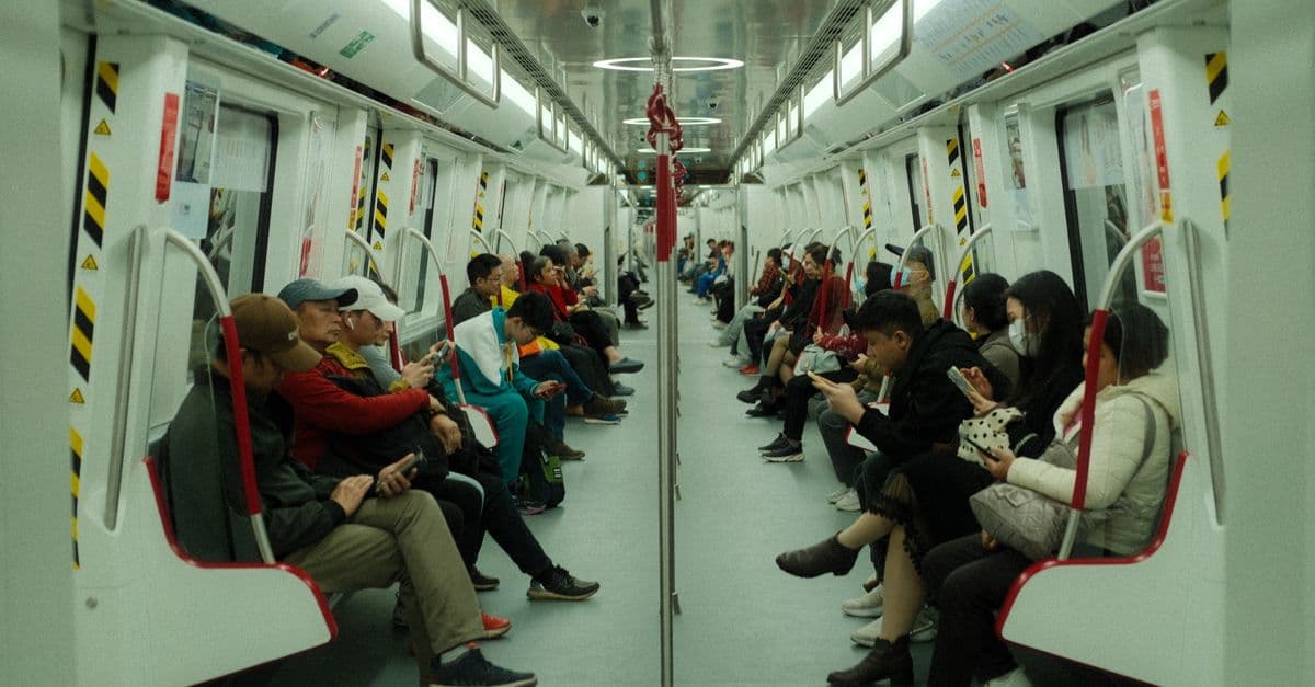 Passengers on a modern subway train using smartphones during daytime commute.