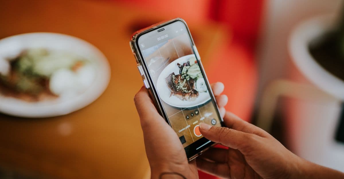 Close-up of a person using a smartphone to photograph food in a cozy indoor setting.
