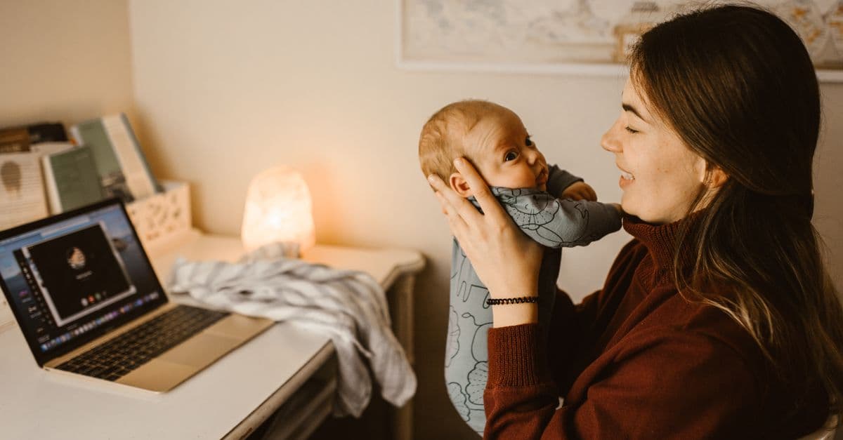 Mother holding baby while video calling from home office. Cozy and heartwarming indoor scene.